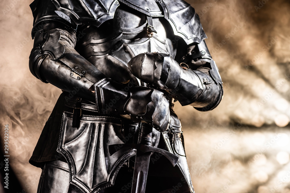 cropped view of knight in armor holding sword on black background cropped view of knight in armor holding sword on black background
