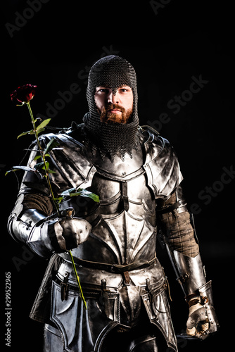 handsome knight in armor holding rose isolated on black