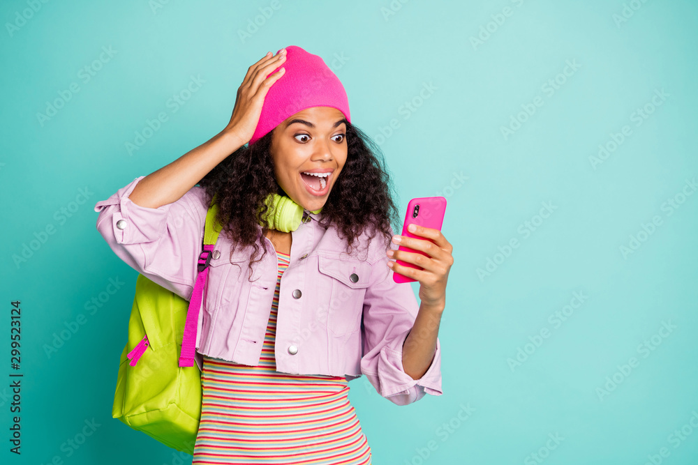 Photo of cheerful positive cute nice sweet casual omg rucksack bag girlfriend excited about reading perfect feedback from audiences in striped t-shirt pink jacket in headphones cap headwear isolated - obrazy, fototapety, plakaty 