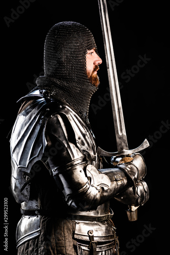 side view of handsome knight in armor holding sword isolated on black