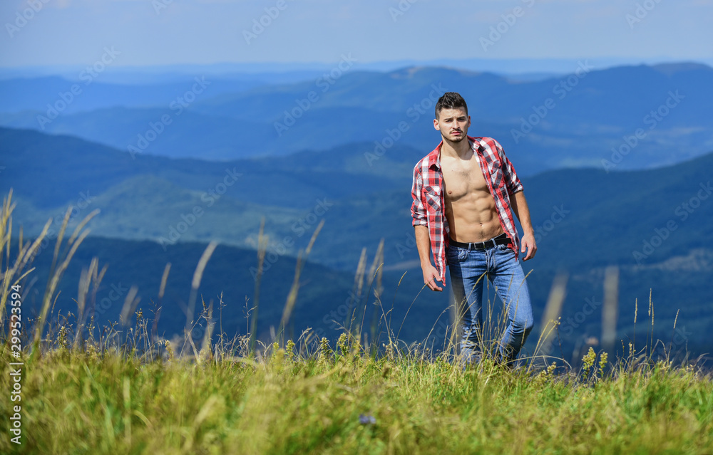 Naklejka premium Muscular tourist walk mountain hill. Hiker muscular torso reach mountain peak. Athlete guy relax mountains. Beautiful environment. Hiking concept. Man stand top mountain landscape background