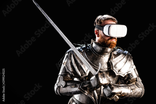 knight with virtual reality headset in armor holding sword isolated on black