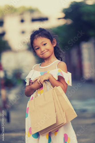 Portrait of beautiful smiling little girl wearing a dress with shopping bag outdoors