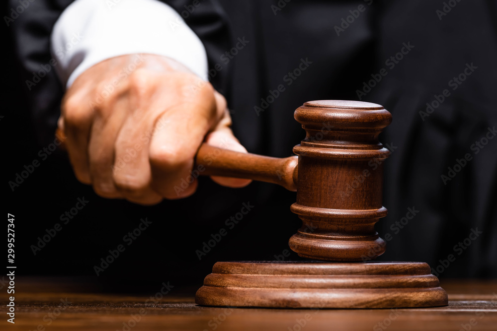 cropped view of judge in judicial robe sitting at table and hitting with gavel - obrazy, fototapety, plakaty 