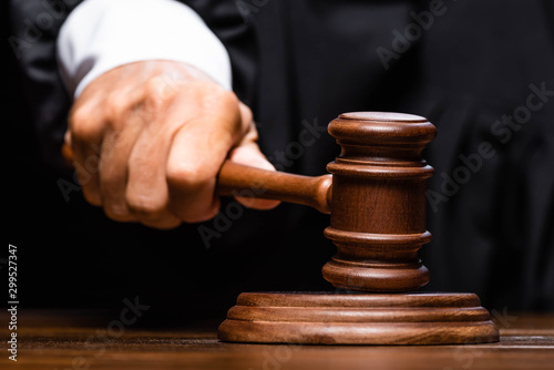 Fototapet cropped view of judge in judicial robe sitting at table and hitting with gavel
