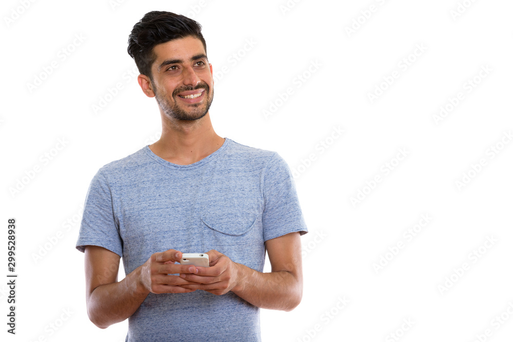 Studio shot of young happy Persian man smiling while holding phone Studio shot of young happy Persian man smiling while holding phone