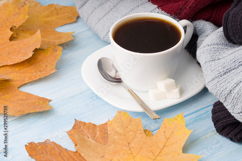 Coffee cup, sweater and autumn leaves. On blue wooden background