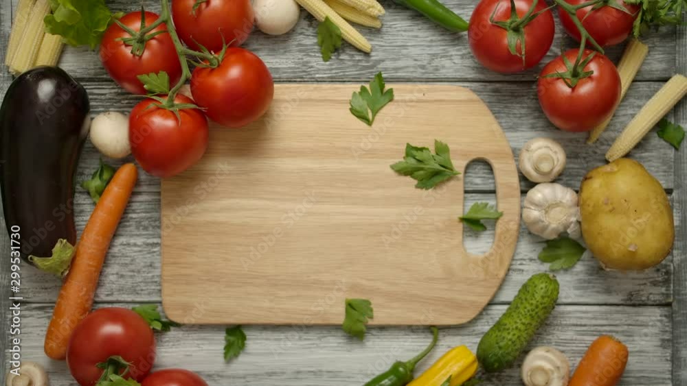 Parsley pieces falling on a cutting board in slow motion with vegetables around. Healthy vegetarian food concept. Nutritious products on a gray wooden table. Vertical camera shooting Parsley pieces falling on a cutting board in slow motion with vegetables around. Healthy vegetarian food concept. Nutritious products on a gray wooden table. Vertical camera shooting