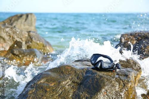black wet diving mask is on the stone in the ocean on the background of splashes of water © Петр Смагин