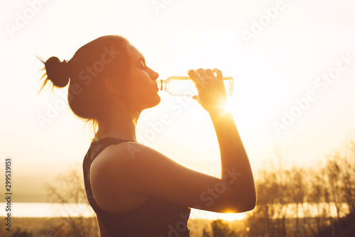Beautiful girl in sportswear drinks water from a bottle at sunset