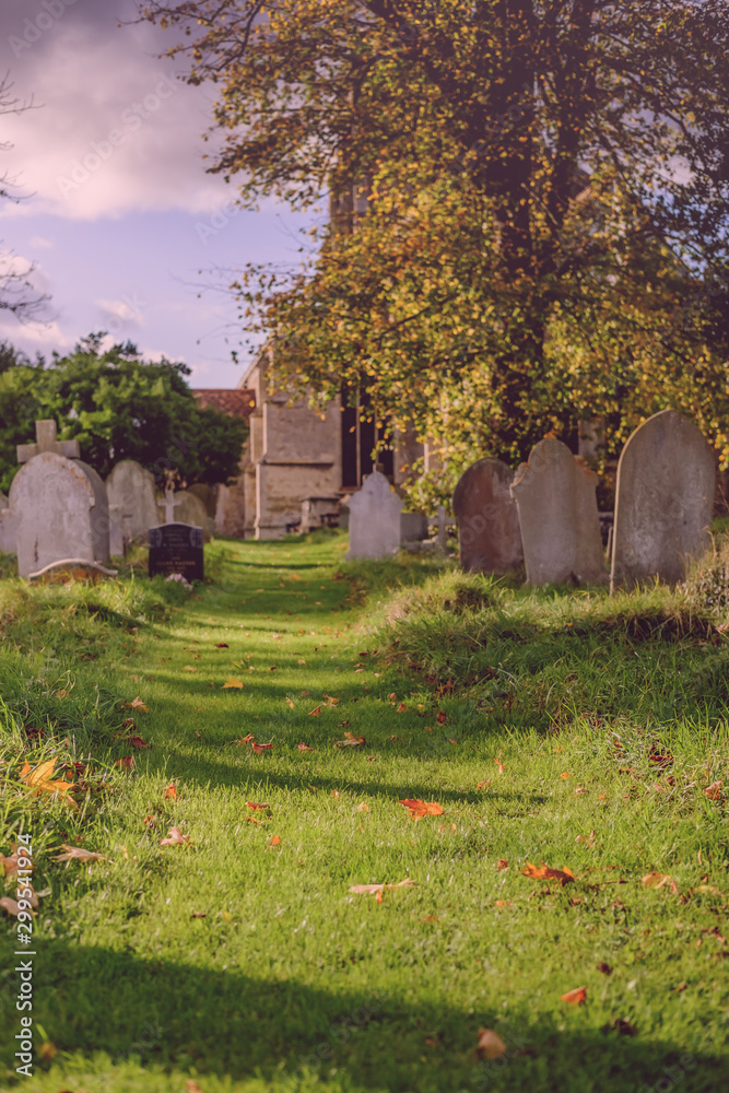  Low level view of the cemetery entrance to an old English church. Thick grass leads the way to the church, with gravestones leading the way.