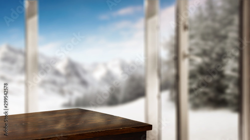 Table corner with space for your product. Blurry winter window with the door open. Beautiful landscape of snowy mountains and festive fir with snow covered branches. Place for your products or inscrip