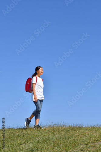 青空で歩く小学生の女の子（ランドセル）