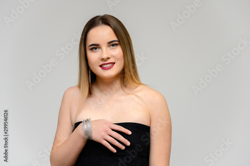 Studio portrait of a beautiful girl with long beautiful hair and excellent make-up on a gray background in different poses. She smiles.