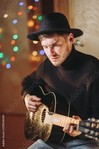 a man in a hat plays the guitar on a background of lights