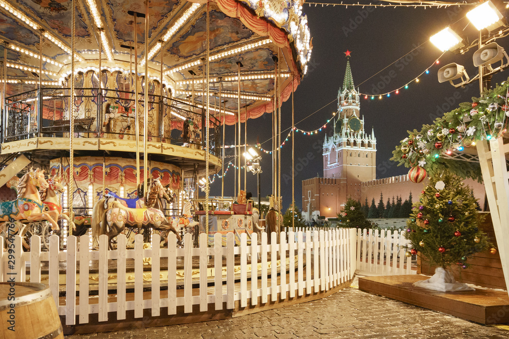 Riding around a horses carousel in winter night located on the Moscow Red Square. Chrismas Eve and New Year mood. Spasskaya Tower of Moscow Kremlin as background.