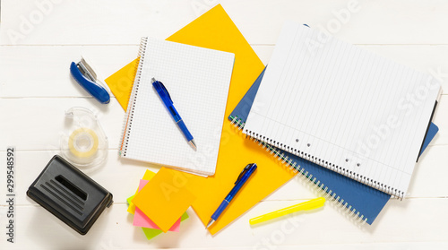 Notepad with pens and stickers. Notebook, pen, books, and pencil holder in the shape of shoe on the white wooden table. Place for text.