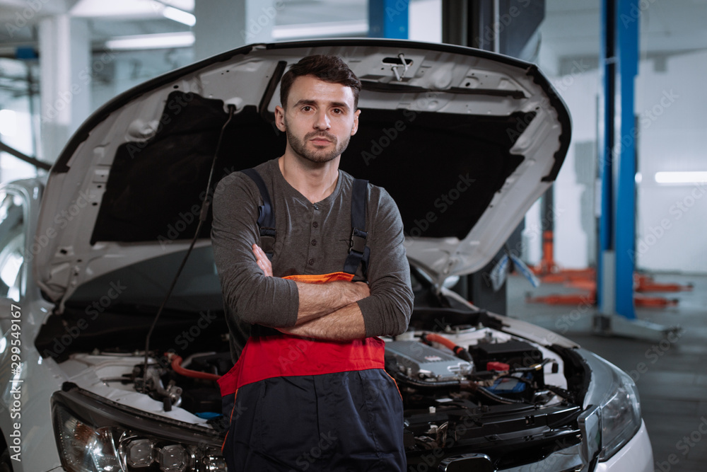 Mechanic man in a uniform seriously in front of the camera in a modern auto service center Mechanic man in a uniform seriously in front of the camera in a modern auto service center