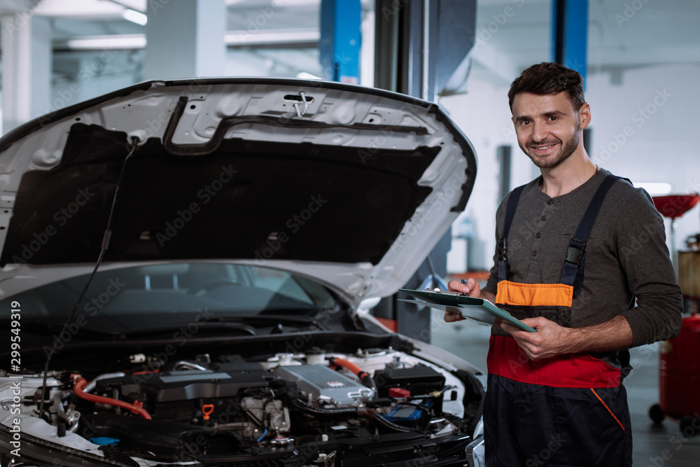 Mechanic man in a uniform smiling large in front of the camera in a modern auto service center Mechanic man in a uniform smiling large in front of the camera in a modern auto service center
