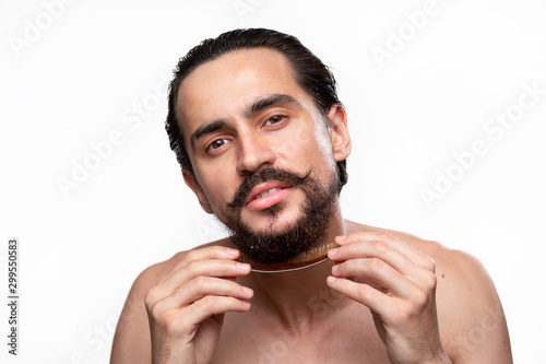 Stylish handsome bearded with mustaches brushing his beard isolated over white background. Concept of morning treatment. Morning routine
