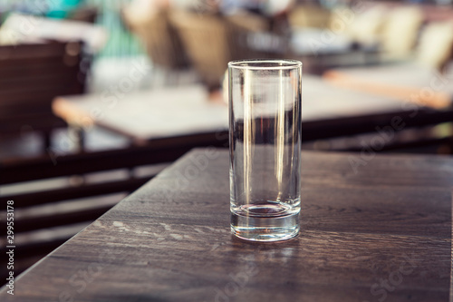 Empty transparent cylindrical glass over wooden table at restaurant, outdoor terrace, extreme shallow of depth field,space for copy text