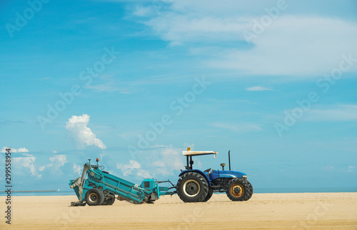 tractor on the sandy beach cleaning, excavator working on sand dunes, Tractor Smoothing The Sand on Public Beach, blue tractor from one side