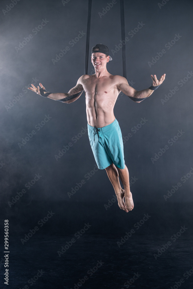 Circus artist on the aerial straps with Strong muscles on black background wearing casual clothes 