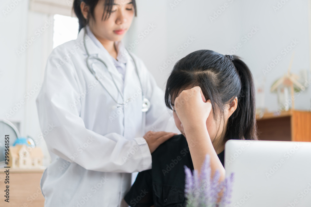 Young patient serious headache siiting on table, Asian female doctor talking for comforting for peace of mind, Medicine student treatment in hospital concept Young patient serious headache siiting on table, Asian female doctor talking for comforting for peace of mind, Medicine student treatment in hospital concept