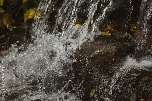 Waterfall from stones in the park. Against the background of autumn foliage and trees of orange and yellow.