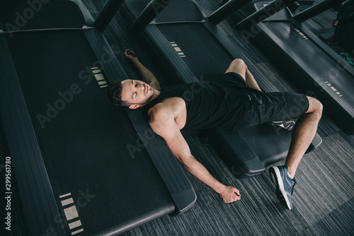 top view of unconscious sportsman lying on treadmill in gym