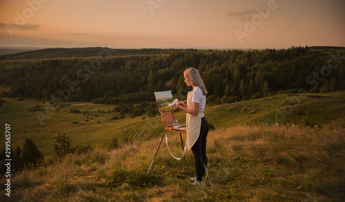 The artist paints a picture outdoors in the early sunny morning. Painting in nature.