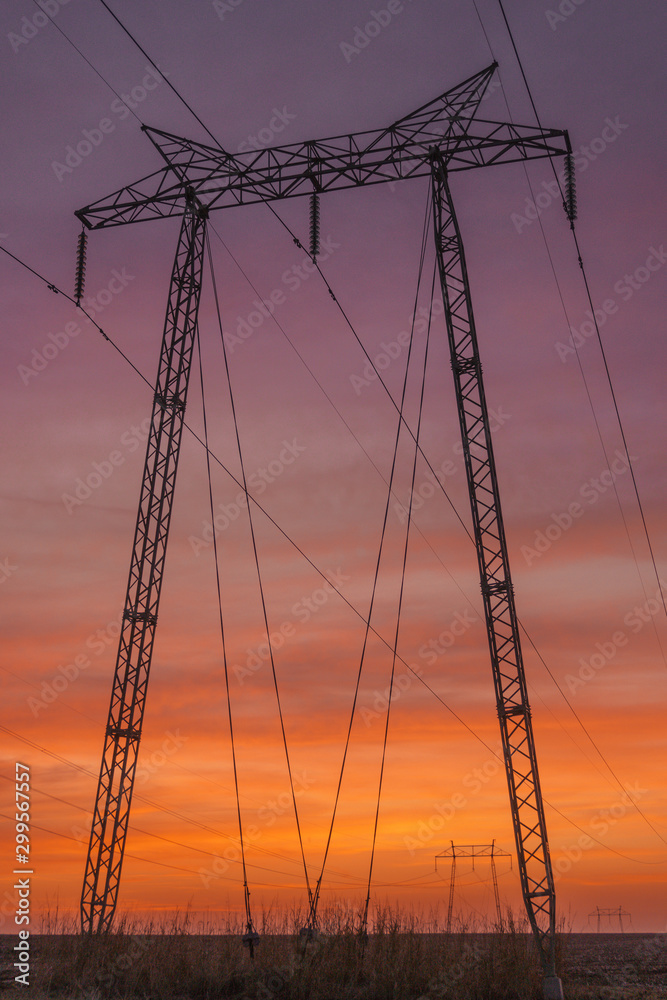 High voltage power towers standing strong in the rays of th e setting sun, under vivid colourful skies