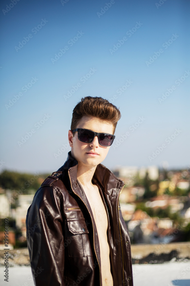 Young attractive man posing in front of camera in a dark brown jacket on the roof of a residential building Young attractive man posing in front of camera in a dark brown jacket on the roof of a residential building