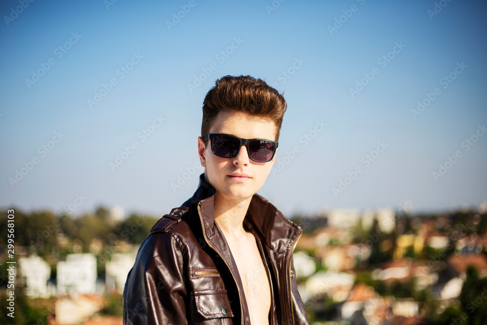 Young attractive man posing in front of camera in a dark  brown jacket on the roof of a residential building