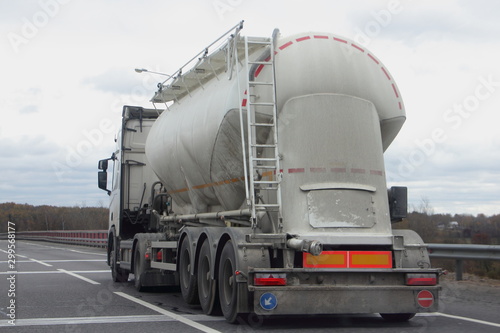 Cement truck with a round barrel semi trailer moving on asphalted highway road in autumn day, Logistics, bulk material road carriage, side rear view