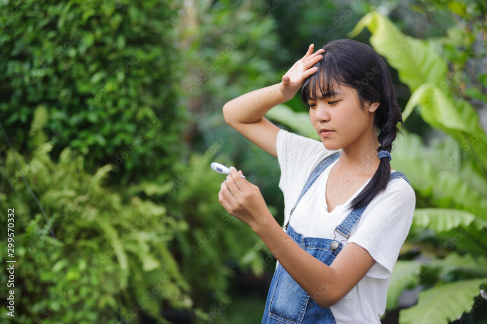 asian teenager woman with pigtail hairs in white shirt looking at thermometer and hands holding a digital thermometer in the garden asian teenager woman with pigtail hairs in white shirt looking at thermometer and hands holding a digital thermometer in the garden
