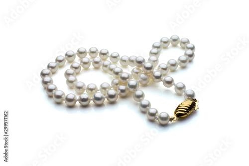 A single strand necklace of white pearls with a gold clasp are crossed over itself. Shown on a white background with shadow.