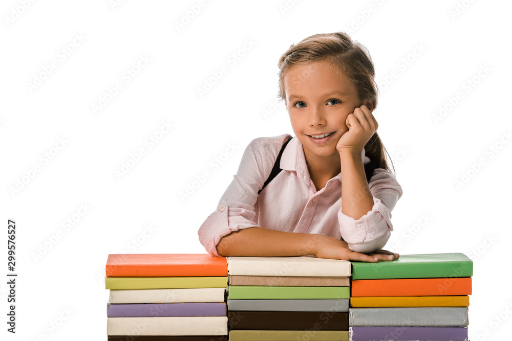 cheerful pupil smiling while looking at camera near colorful books isolated on white cheerful pupil smiling while looking at camera near colorful books isolated on white
