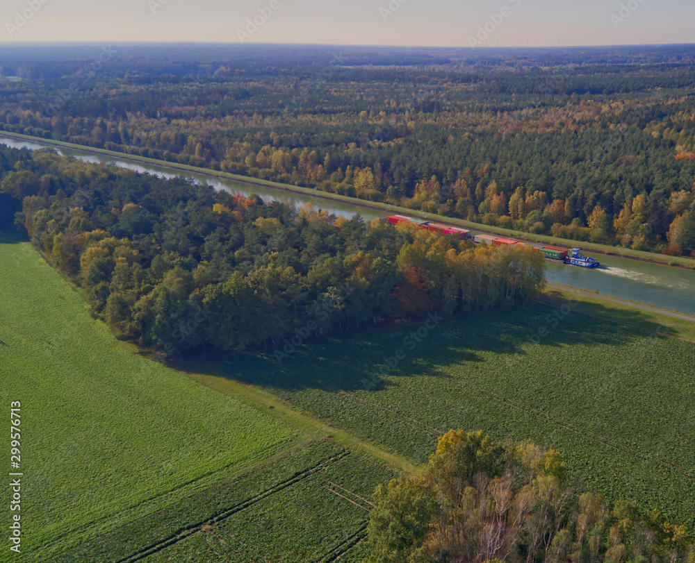 View from a height of 100 meters over the flat landscape in northern Germany with a canal and a canal ship transporting containers.