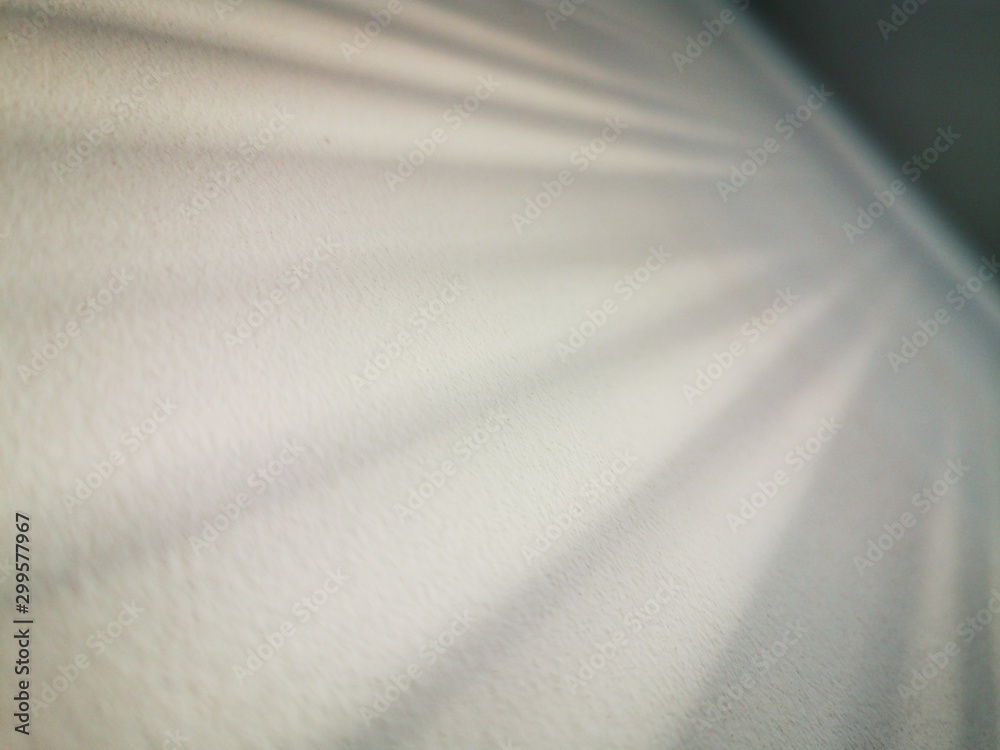 The shadow of the blinds on a white wall. Abstract monochrome pattern. The rays of reflected sun rays.