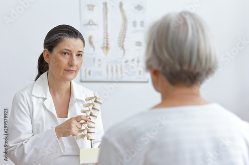 Aging and back pain concept: doctor of orthopedics showing her senior patient a slipped disk on a backbone model.
