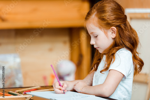 cute redhead child holding color pencil while drawing on paper