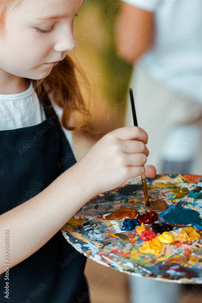 selective focus of redhead child holding paintbrush and palette in art school selective focus of redhead child holding paintbrush and palette in art school