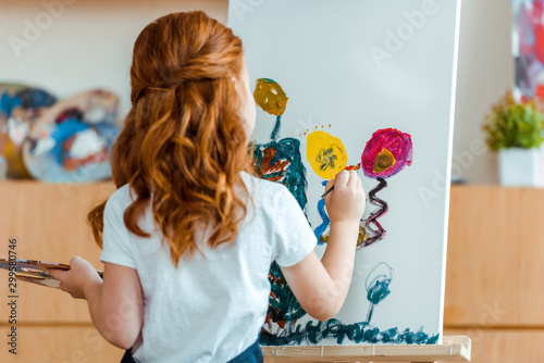 back view of redhead child painting on canvas in art school