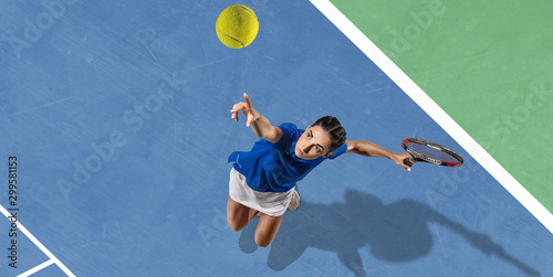 Young caucasian brunette woman in blue shirt playing tennis at the court. Hits ball with racket, outdoors. Youth, flexibility, power, energy. Copyspace. Top view. Motion, action, healthy lifestyle.