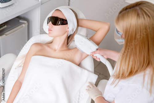 Young pretty caucasian woman in dark glasses is undergoing photoepilation procedure in the salon. Concept removal of unwanted hair from body skin