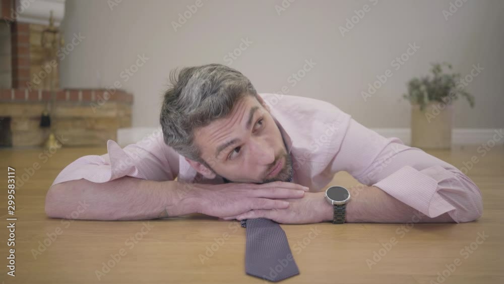 Portrait of henpecked husband or boyfriend laying on the floor. Beautiful female legs in red high-heel shoes passing by at the foreground. Sad handsome gray-haired Caucasian man controlled by spouse. Portrait of henpecked husband or boyfriend laying on the floor. Beautiful female legs in red high-heel shoes passing by at the foreground. Sad handsome gray-haired Caucasian man controlled by spouse.
