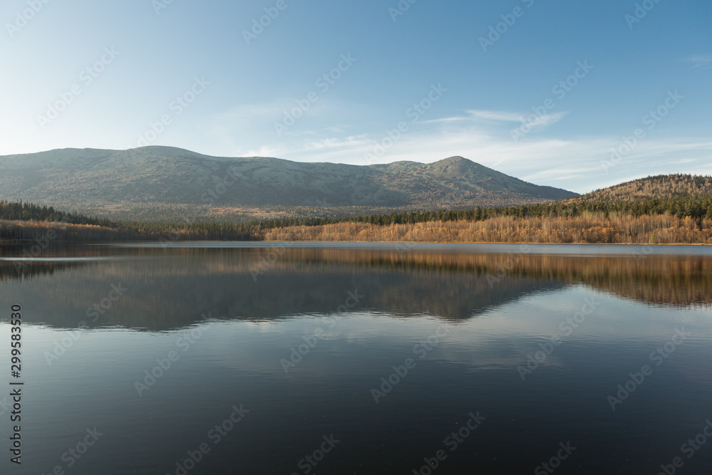 Autumn landscape in the mountains. Reflection of mountains and yellow, green trees on the surface of the lake. Russia. Siberia.