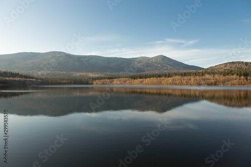 Autumn landscape in the mountains. Reflection of mountains and yellow, green trees on the surface of the lake. Russia. Siberia.