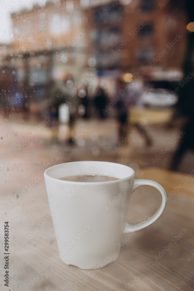 Woman hand holding the cup of coffee or tea on rainy day window background in vintage color tone, copy space